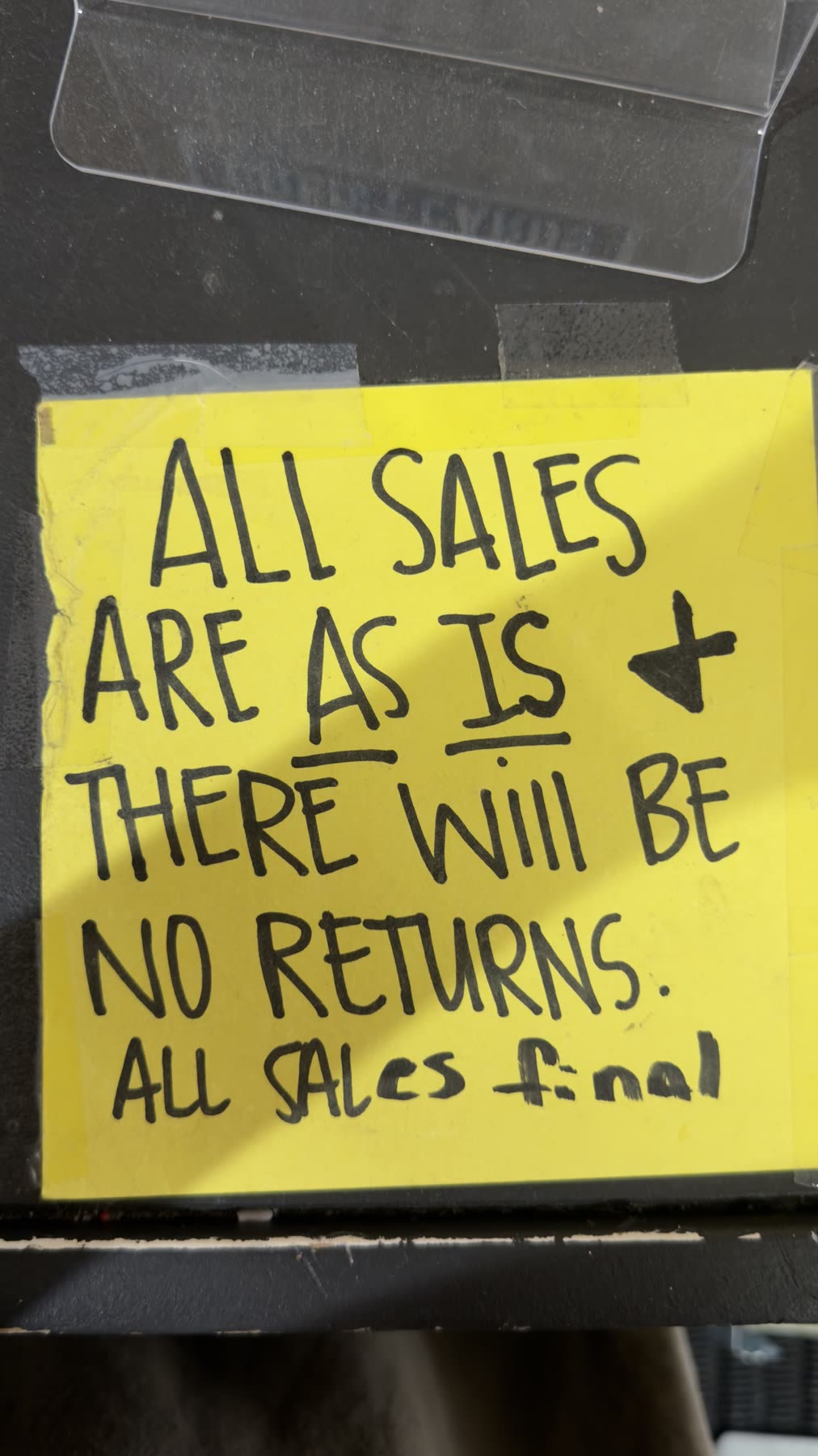 Handwritten yellow sign reading All sales are as is, there will be no returns, all sales final
