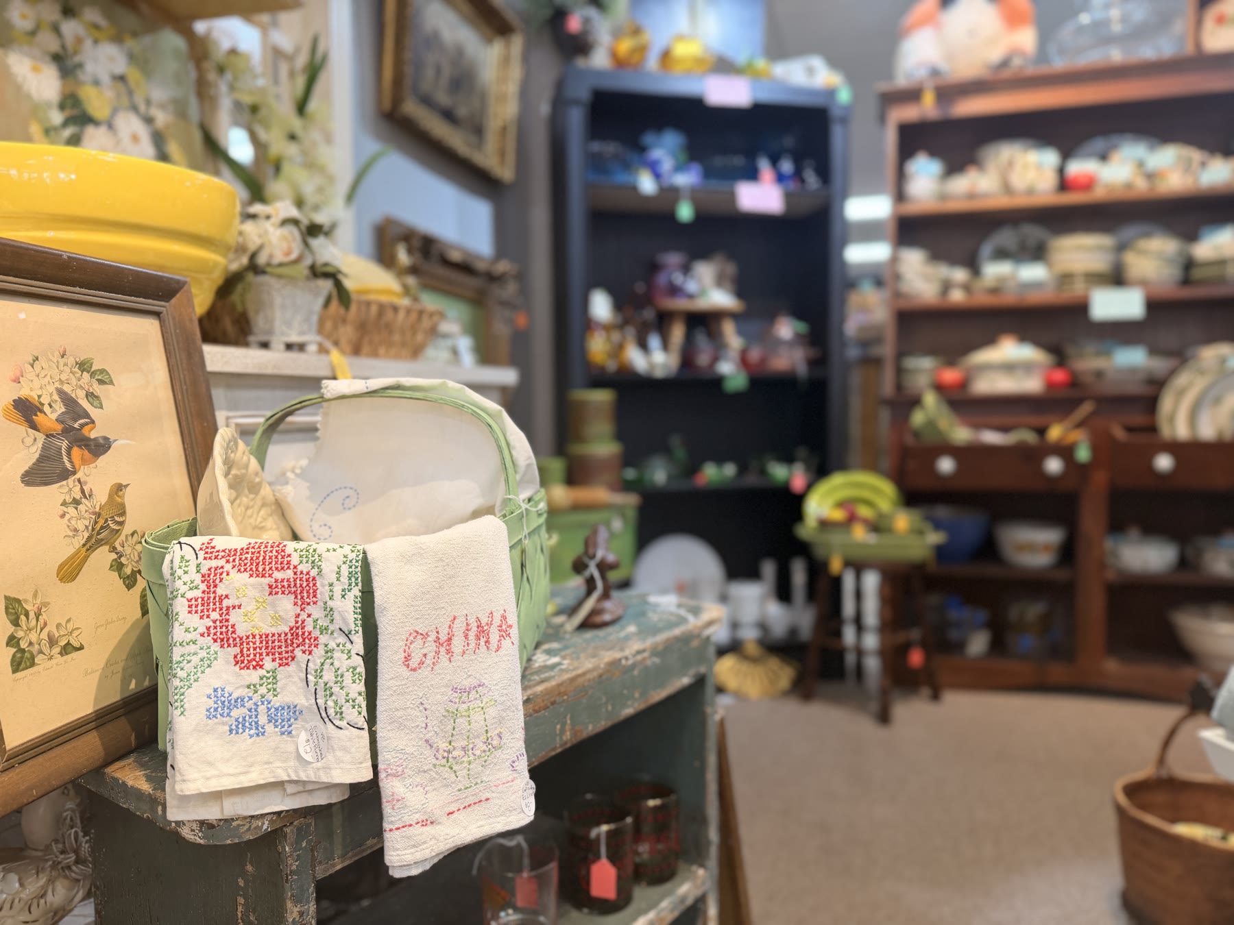 Cross-stitched China linens on a green-painted shelf with a bird print
